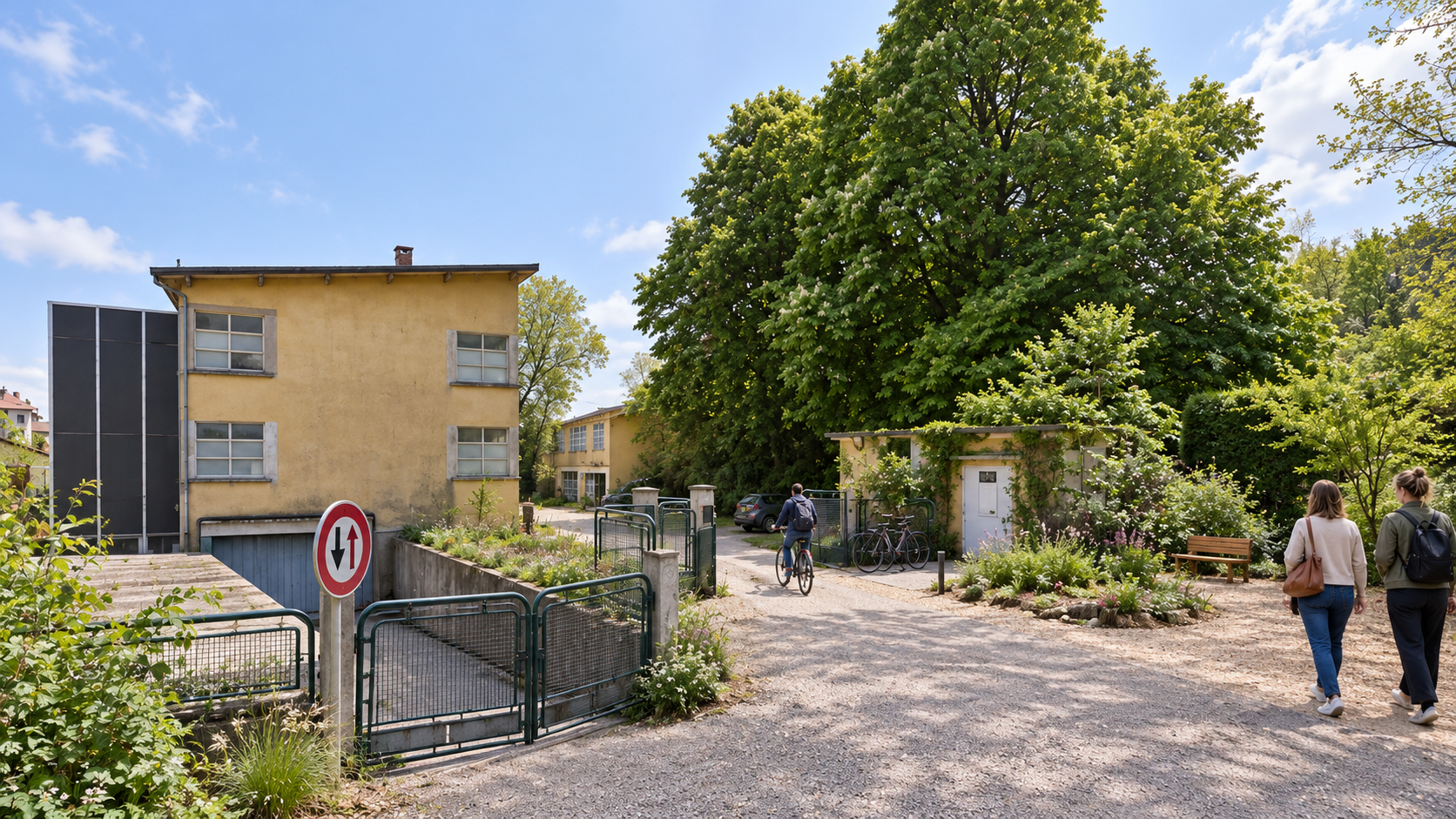 Vue extérieure du site de l'usine STPS : bâtiment jaune, cour en gravier, arbres et cheminements piétons.
